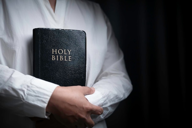 Faith with holy bible concept Hands of a female prayer worship God with holy bible on black background in church Christian woman who believe in Jesus read and study the grace of the holy scriptures