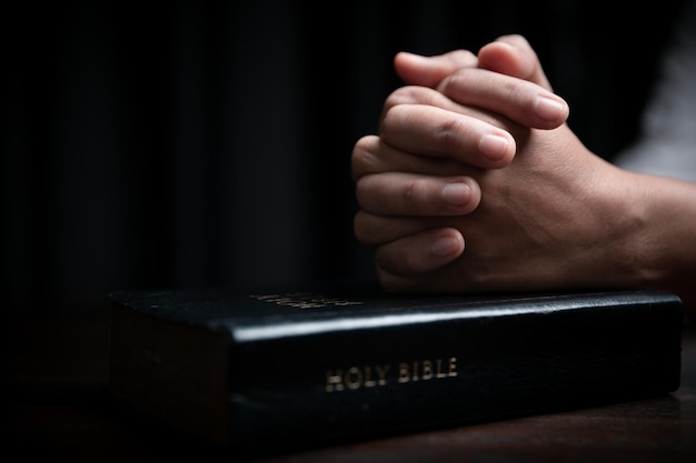 Faith with holy bible concept Hands of a female prayer worship God with holy bible on black background in church Christian woman who believe in Jesus read and study the grace of the holy scriptures