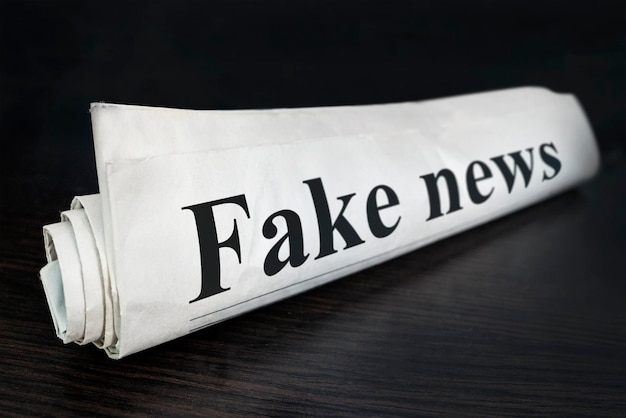 Fake News Newspaper on desk in the office Daily news newspaper headline reading fake news concept for false event news headline Rolled Up Newspaper concept of false deceit falsehood