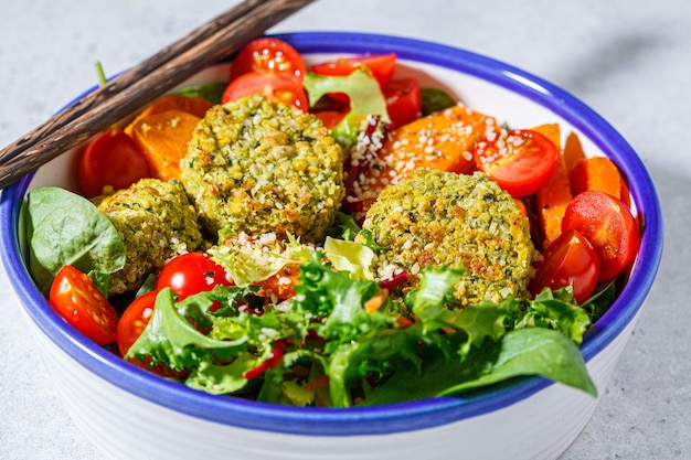 Falafel salad with baked vegetables and tomatoes in a white bowl. Israeli street food concept.