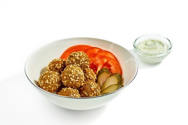 Falafel with cucumbers and tomatoes in a white bowl white garlic sauce isolated on a white background