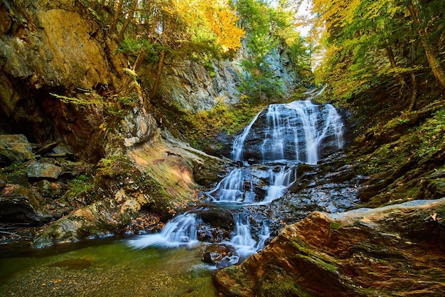 Fall leaves cover rocky gorge with raging waterfall and trees in peak foliage