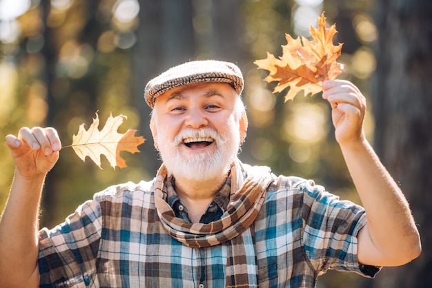 Fallen autumn leaves strewn about the ground elderly man smiling outdoors in nature grandfather havi...