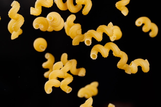 Falling cavatappi pasta. Flying yellow raw macaroni over black background. Shallow dof.