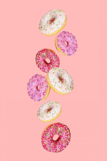 Falling doughnuts with colored glaze on trendy pink background.  Levitating food.