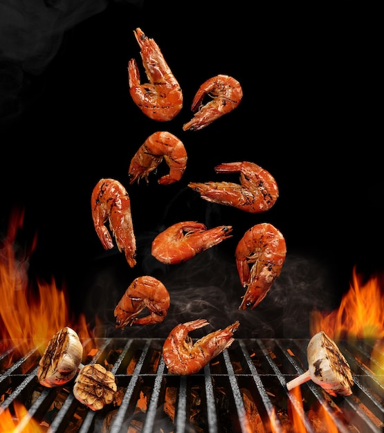 Falling down barbecue bbq grilled shrimps with halves of garlic black background flaming fire ember ...