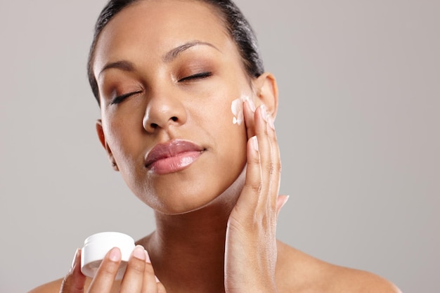 Falling in love with her face cream Cropped shot of a beautiful young woman applying face cream while standing in a studio