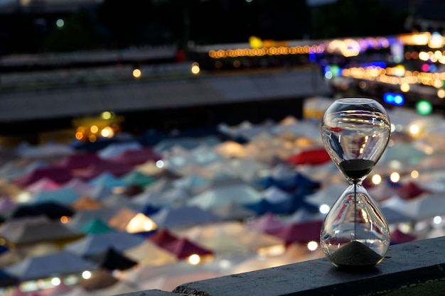 Falling sand in a hourglass with colorful blur market in background