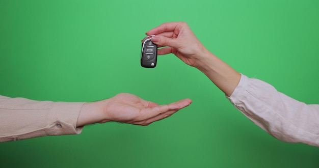 Famale hand gives a car keys to male hand on the green background close up