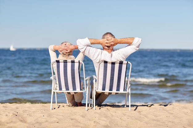 family, age, travel, tourism and people concept - happy senior couple sitting on deck chairs on summer beach