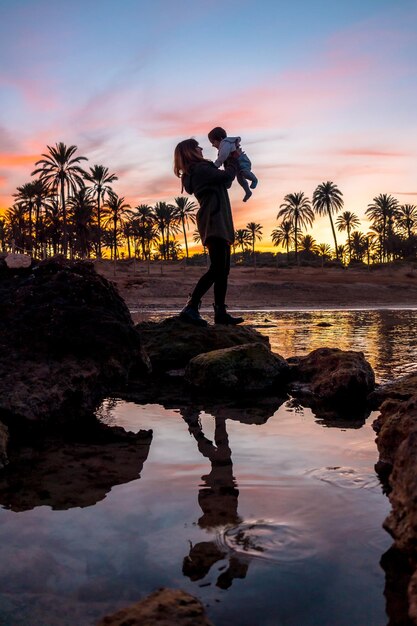 Family on the beach young mother with her baby by the sea at orange sunset