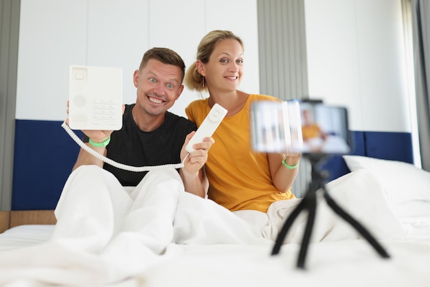 Family of bloggers hold pushbutton phone and shoot video on camera in hotel room blog about