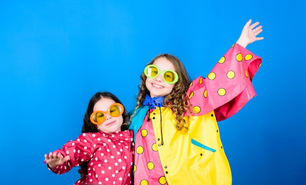 Family bonds Small girls in raincoat and glasses happy small girls in colorful rain coat rain protection Rainbow autumn fashion cheerful hipster children sisterhood having fun Totally free