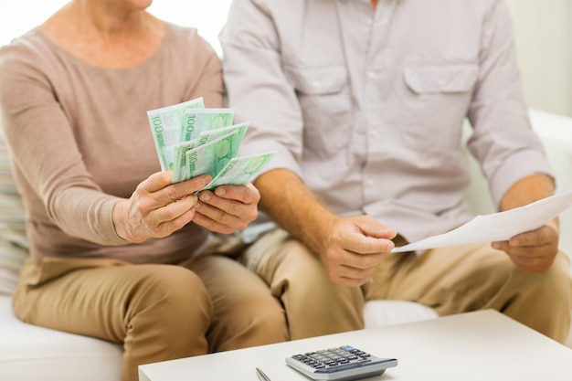 family, business, savings age and people concept - close up of senior couple with papers, money and calculator at home