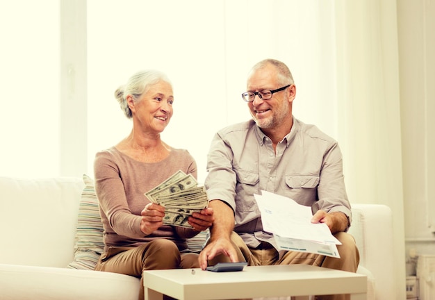 family, business, savings, age and people concept - smiling senior couple with papers, money and calculator at home