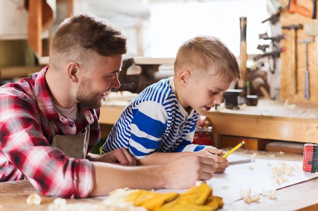 Photo family, carpentry, woodwork and people concept - happy father and little son with blueprint at workshop