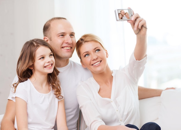 family, child, photography and home concept - happy family with little girl making self portrait with digital camera