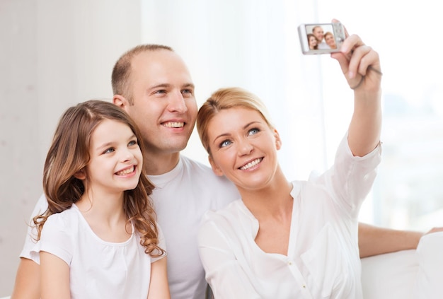 family, child, photography and home concept - happy family with little girl making self portrait with digital camera