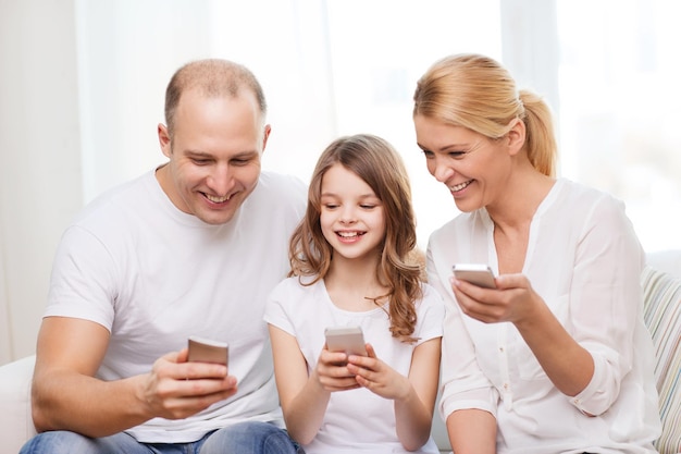 family, child, technology and home concept - smiling parents and little girl with smartphones at home