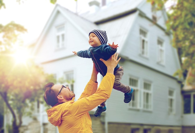 family, childhood, fatherhood, leisure and people concept - happy father and little son playing and having fun outdoors over living house background