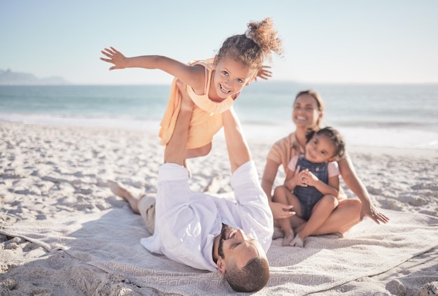 Family children and playing with a girl on a beach holiday with her parents and sister during summer Kids travel and ocean with a female child or daughter on the sand by the sea with her father