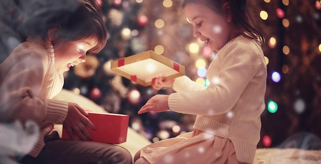 Family on Christmas eve at fireplace Kids opening Xmas presents Children under Christmas tree with gift boxes Decorated living room with traditional fire place Cozy warm winter evening at home