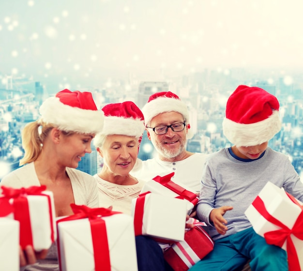 family, christmas, generation, holidays and people concept - happy family in santa helper hats with gift boxes sitting over blue snowy background