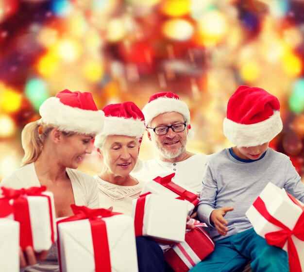 family, christmas, generation, holidays and people concept - happy family in santa helper hats with gift boxes sitting over red lights background