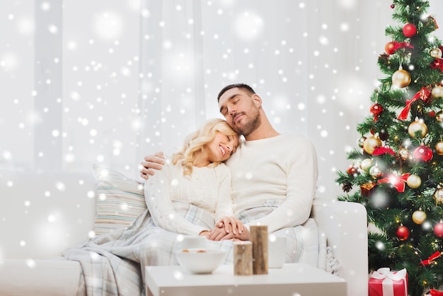 family, christmas, holidays, love and people concept - happy couple covered with plaid sitting on sofa at home