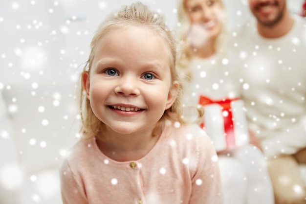 family, christmas, holidays and people concept - happy mother, father and little daughter with gift box sitting on sofa at home