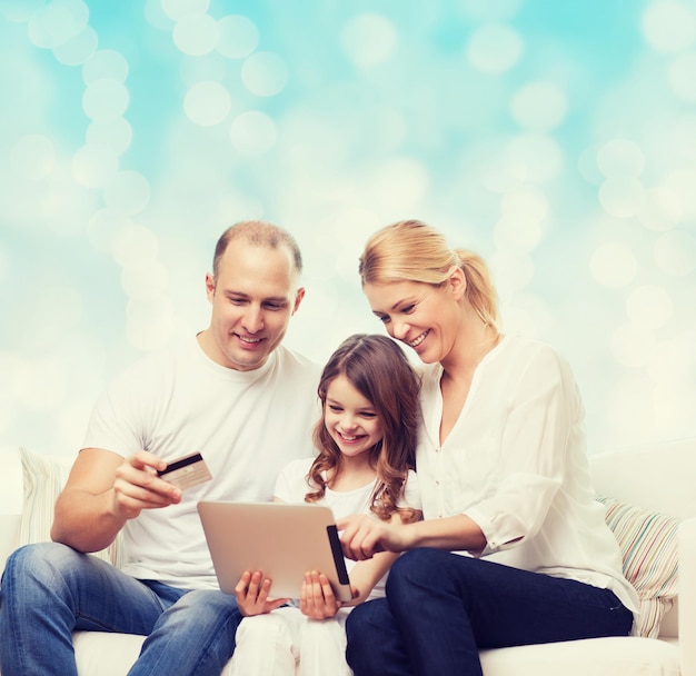 family, christmas holidays, shopping, technology and people - smiling family  with tablet pc computer and credit card over blue lights background