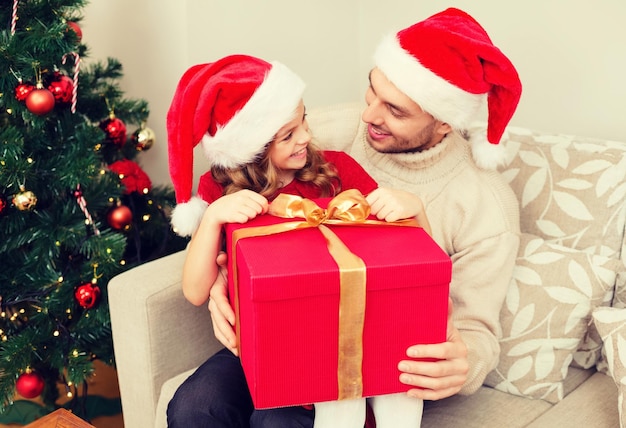 family, christmas, x-mas, happiness and people concept - smiling father and daughter in santa helper hats opening gift box