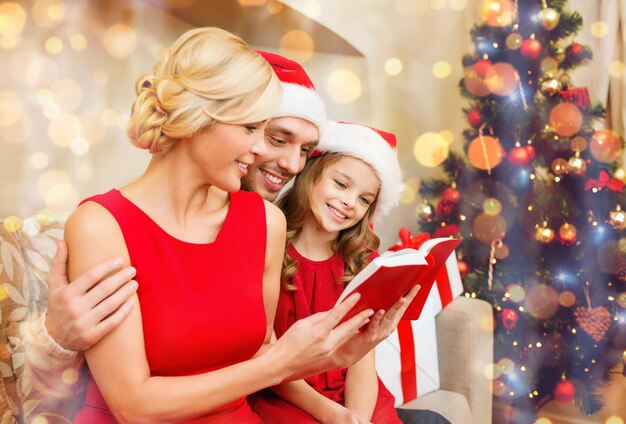 family, christmas, x-mas, winter, happiness and people concept - smiling family in santa helper hats with many gift boxes reading book