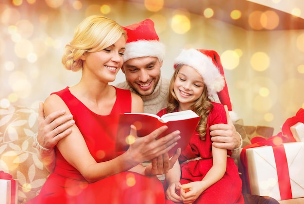 family, christmas, x-mas, winter, happiness and people concept - smiling family in santa helper hats with many gift boxes reading book