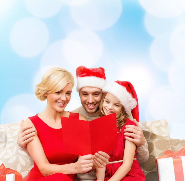 family, christmas, x-mas, winter, happiness and people concept - smiling family in santa helper hats with many gift boxes reading postcard