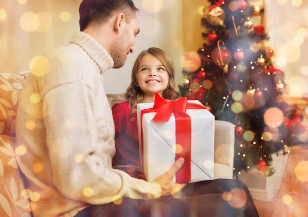 family, christmas, x-mas, winter, happiness and people concept - smiling father and daughter holding gift box and looking at each other