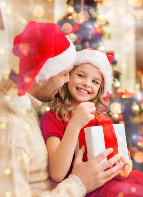 family, christmas, x-mas, winter, happiness and people concept - smiling father and daughter in santa helper hats opening gift box