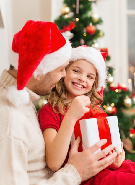 family, christmas, x-mas, winter, happiness and people concept - smiling father and daughter in santa helper hats opening gift box