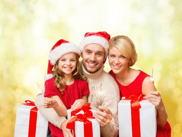 family, christmas, xmas, happiness and people concept - smiling family in santa helper hats with many gift boxes and bengal lights