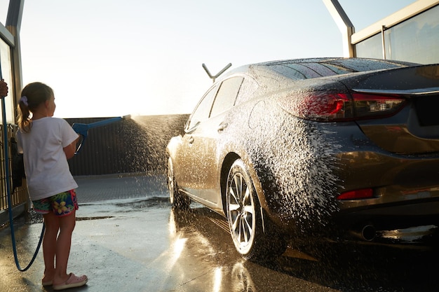 Family cleaning car in selfservice at car wash during sunset Car covered in white foam Concept of easy and fun selfservice