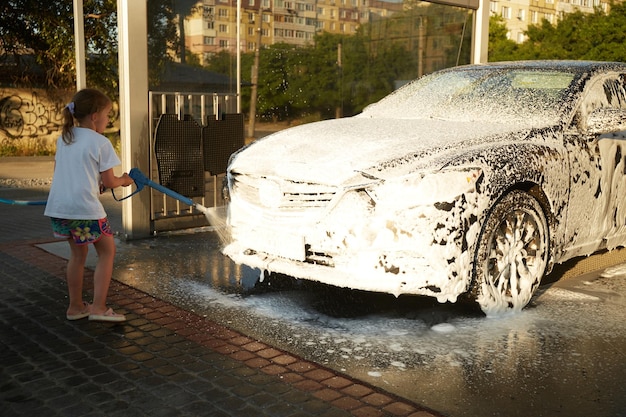 Family cleaning car in selfservice at car wash during sunset Car covered in white foam Concept of easy and fun selfservice