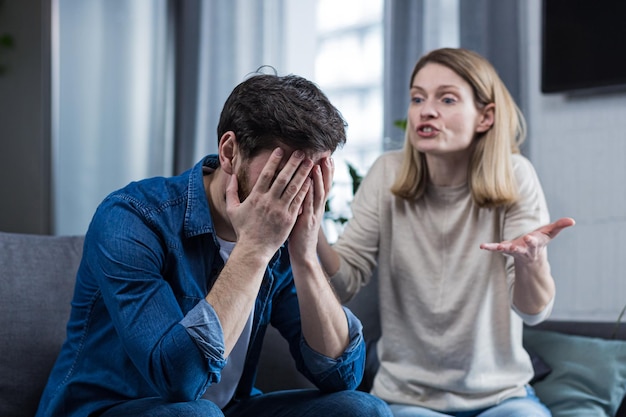 Family conflict quarrel misunderstanding The woman shouts at her husband in despair crying requires explanation The man listens covering his face with his hands Sitting on the couch at home