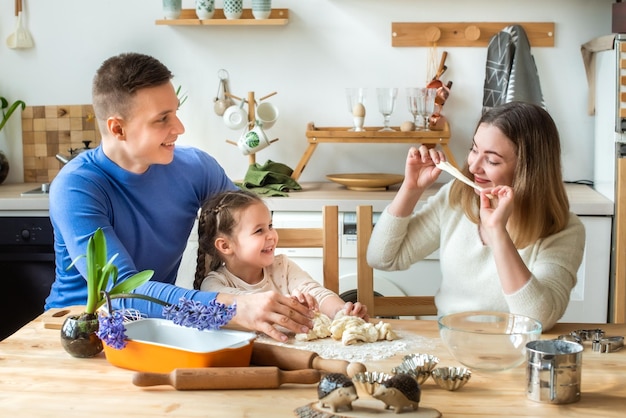 Family cooks at home mom dad and daughter knead the dough in a kitchen man girl woman together