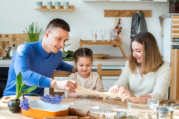 Family cooks at home mom dad and daughter knead the dough in a kitchen man girl woman together