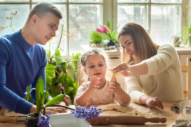 Family cooks at home mom dad and daughter knead the dough in a kitchen man girl woman together