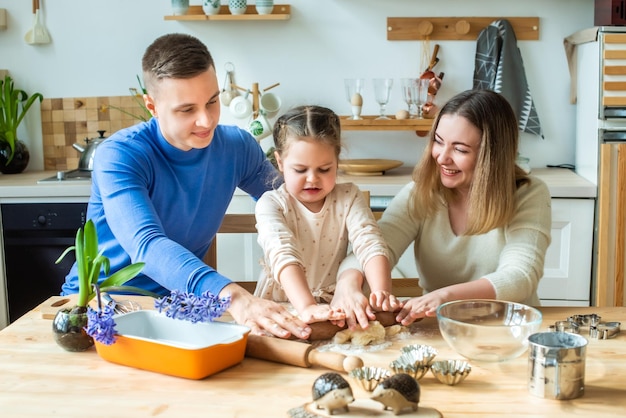 Family cooks at home mom dad and daughter knead the dough in a kitchen man girl woman together