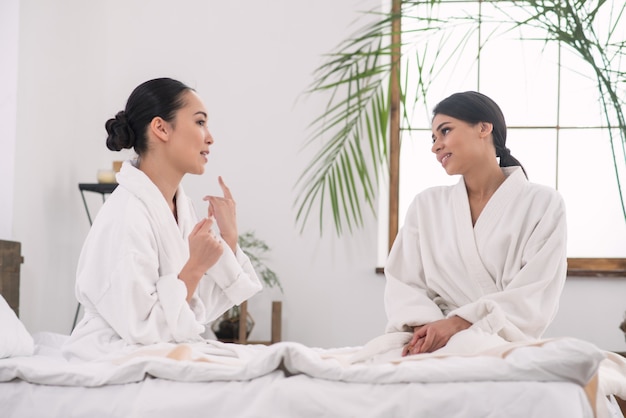 Family day. Positive young sisters being talking to each other while spending time in the spa salon