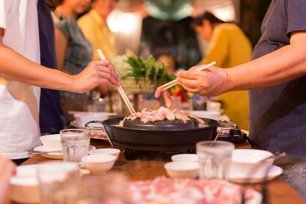 Family dinner hand with chopstick cooking pork slice on hot BBQ pan.