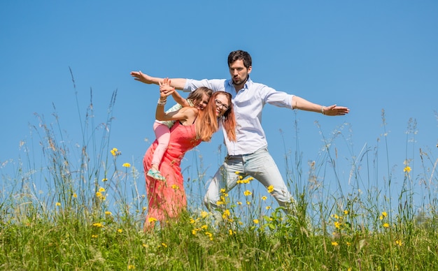 Family doing the plane on summer meadow under clear blue sky