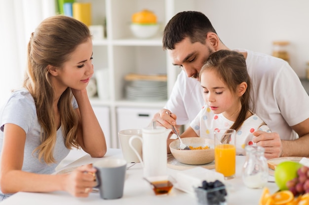 family eating and people concept happy mother father and daughter having breakfast at home